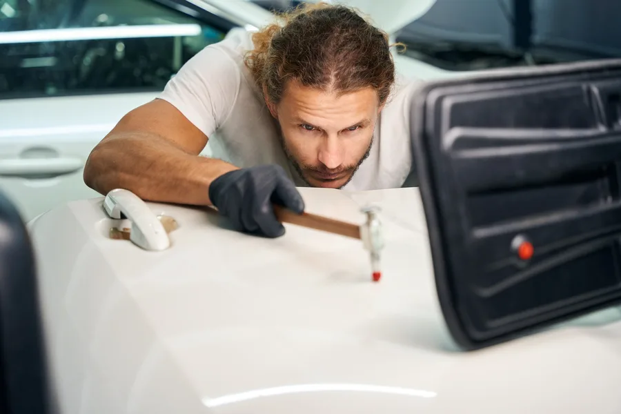 Technician smoothing out dents on the door of a white car